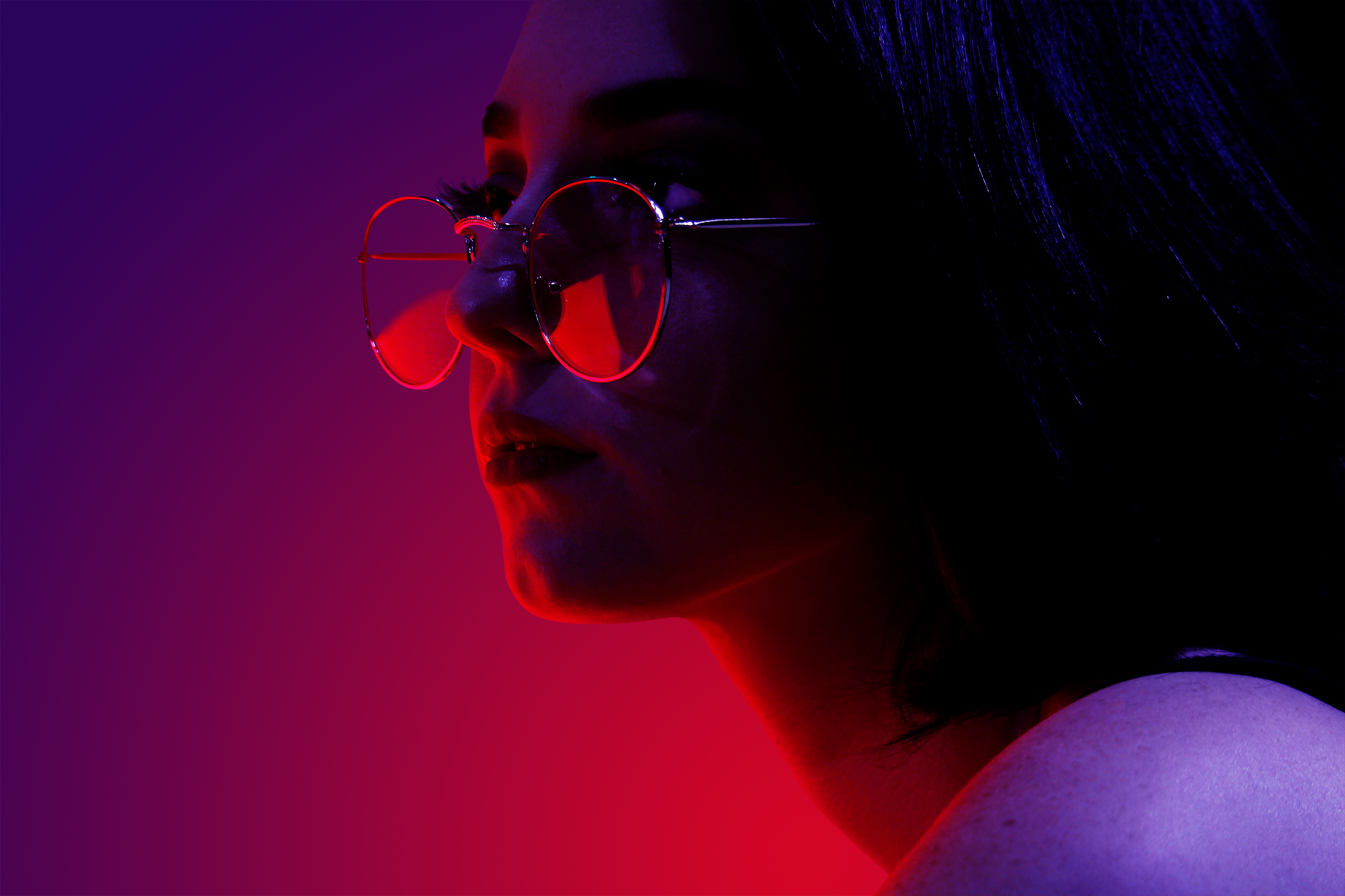 Woman wearing stylish glasses lit with red and purple light.